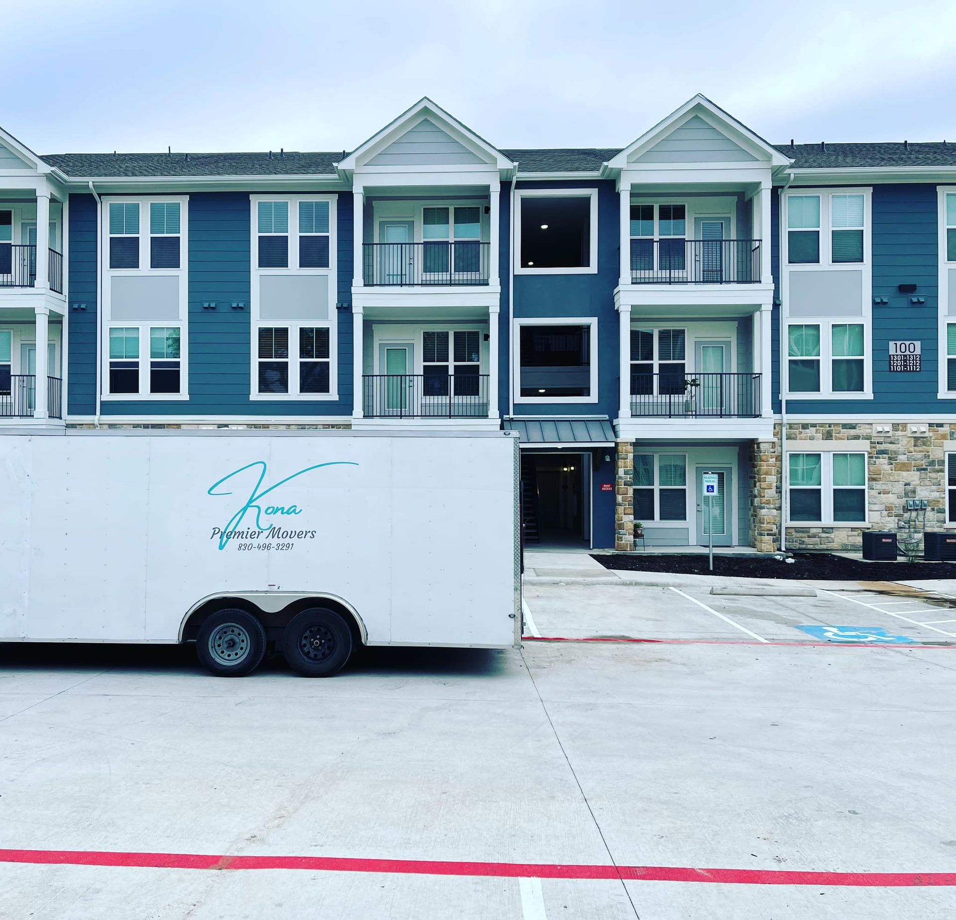 A white trailer is parked in front of a blue apartment building