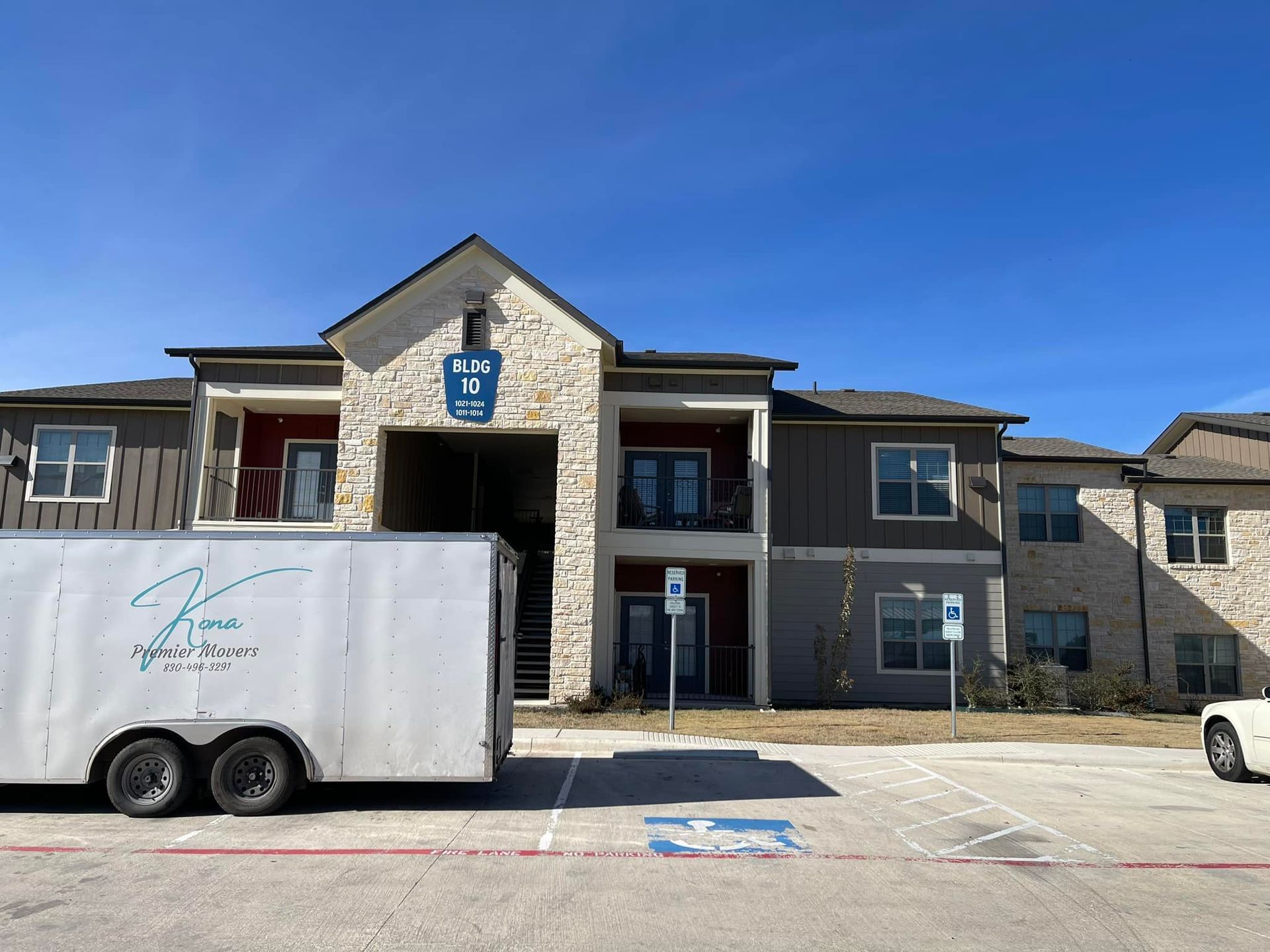 A white trailer is parked in front of a large apartment building.