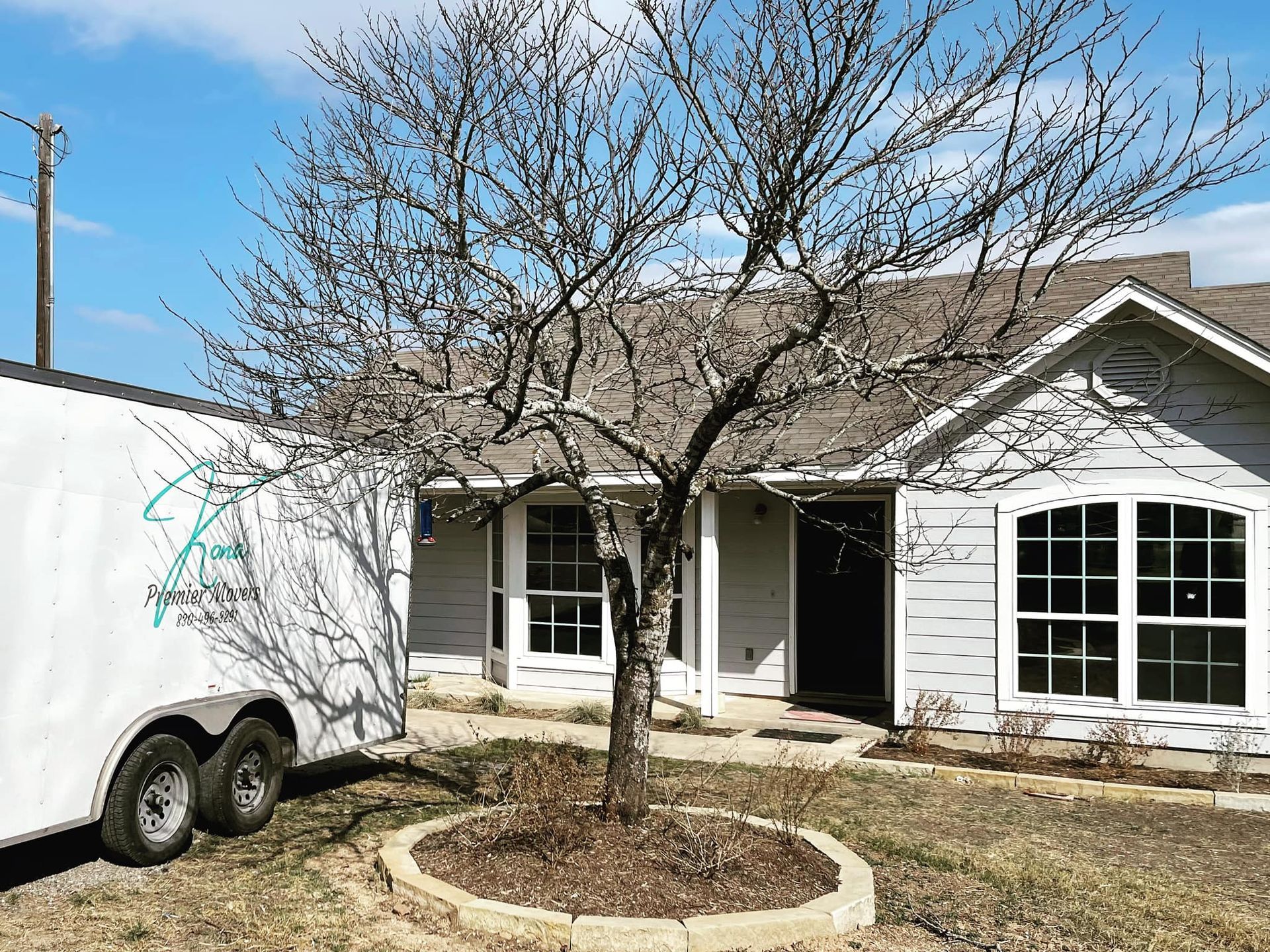 A white trailer is parked in front of a house with a tree in front of it.