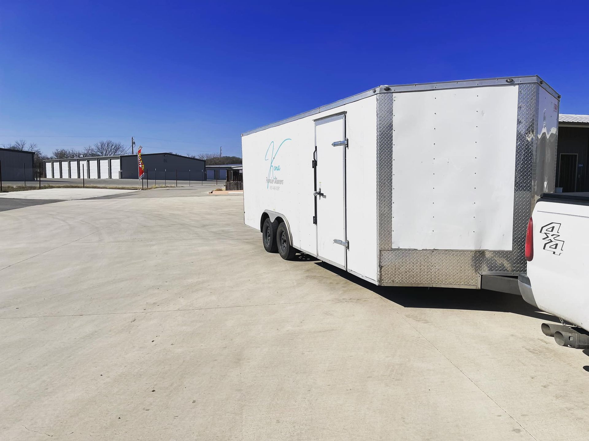 A white trailer is parked next to a white truck in a parking lot.