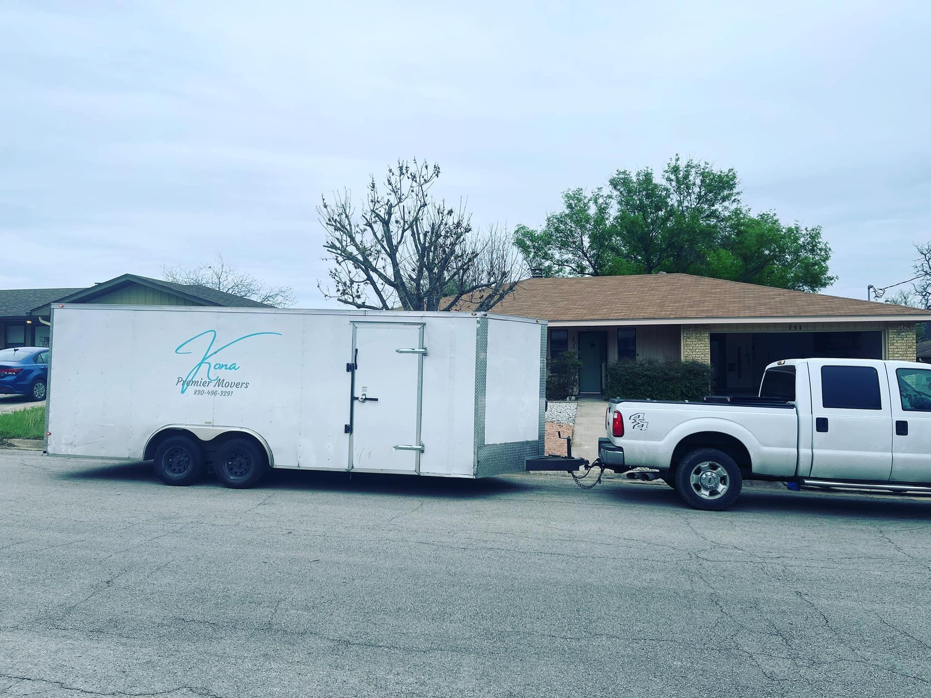A white truck is pulling a trailer in front of a house.