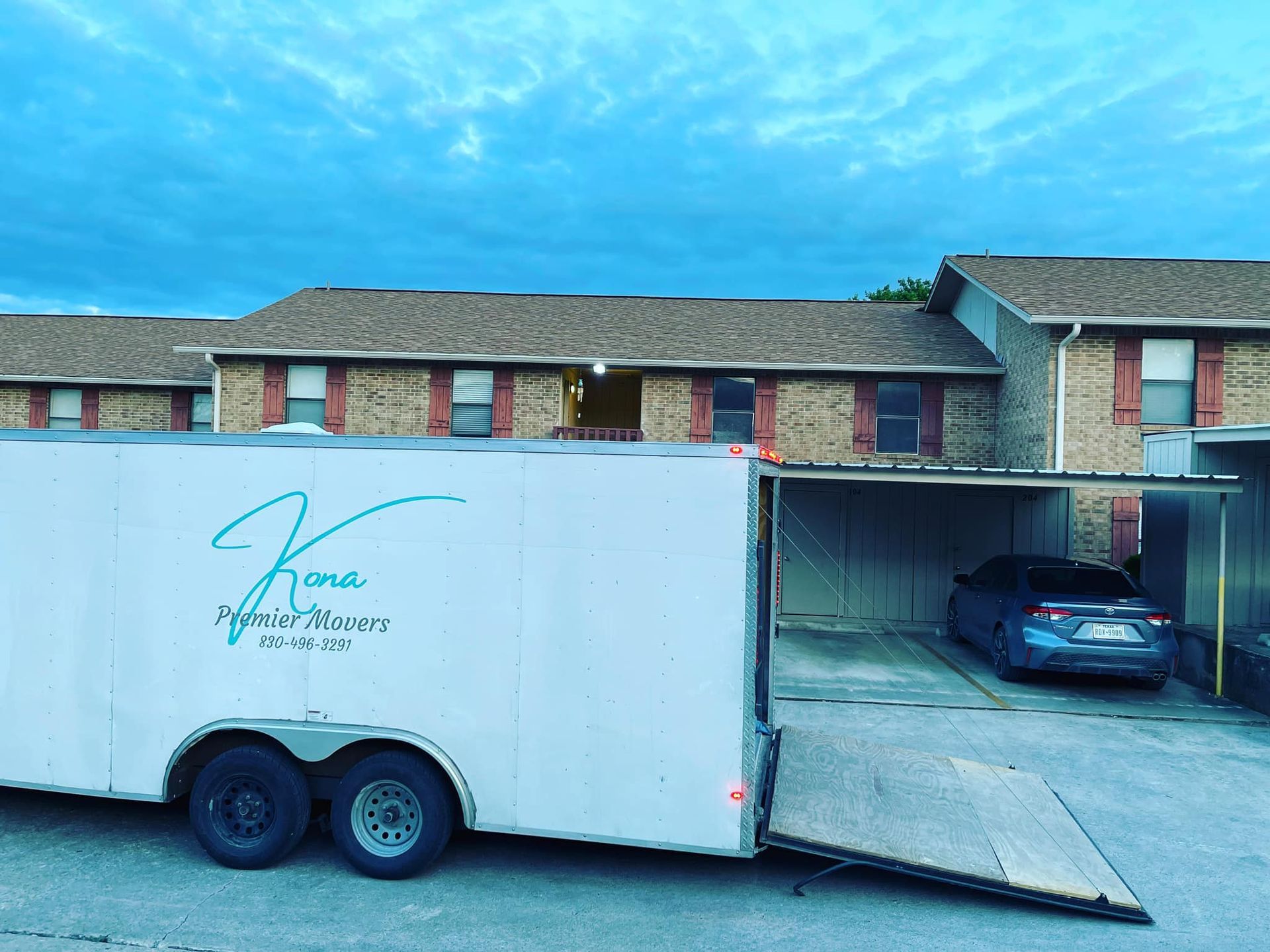 A white trailer is parked in front of a brick apartment building.