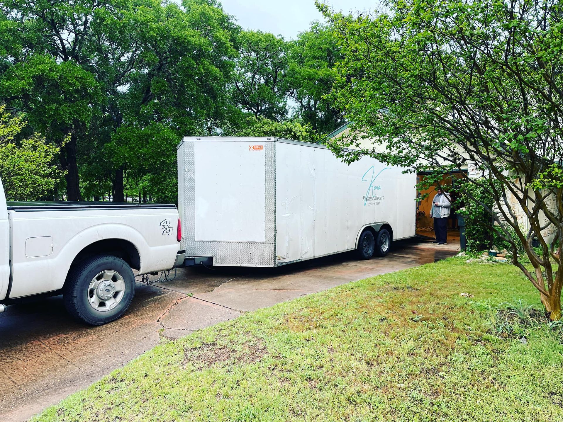 A white truck is towing a white trailer down a dirt road.