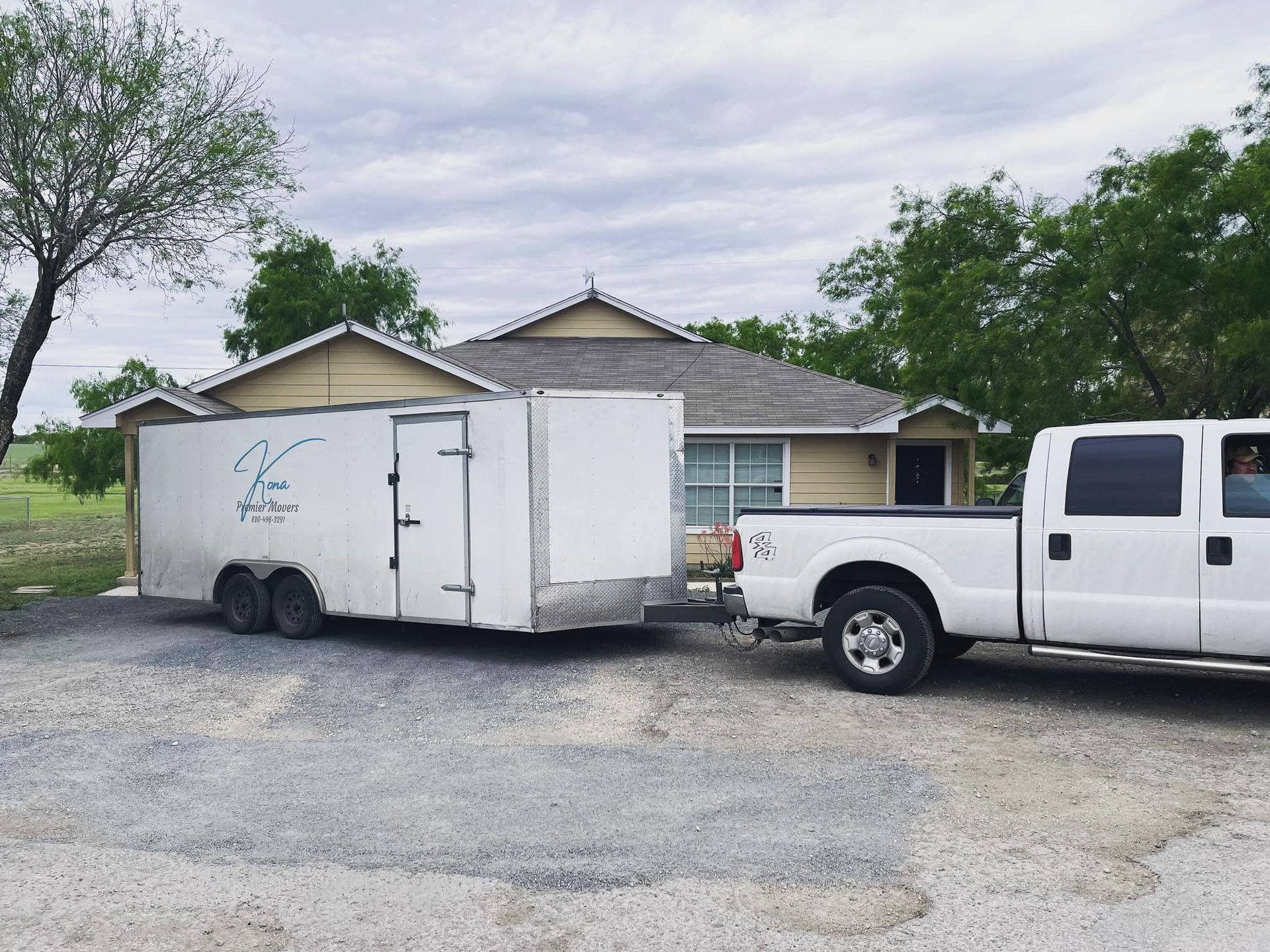 A white truck is pulling a trailer in front of a house.