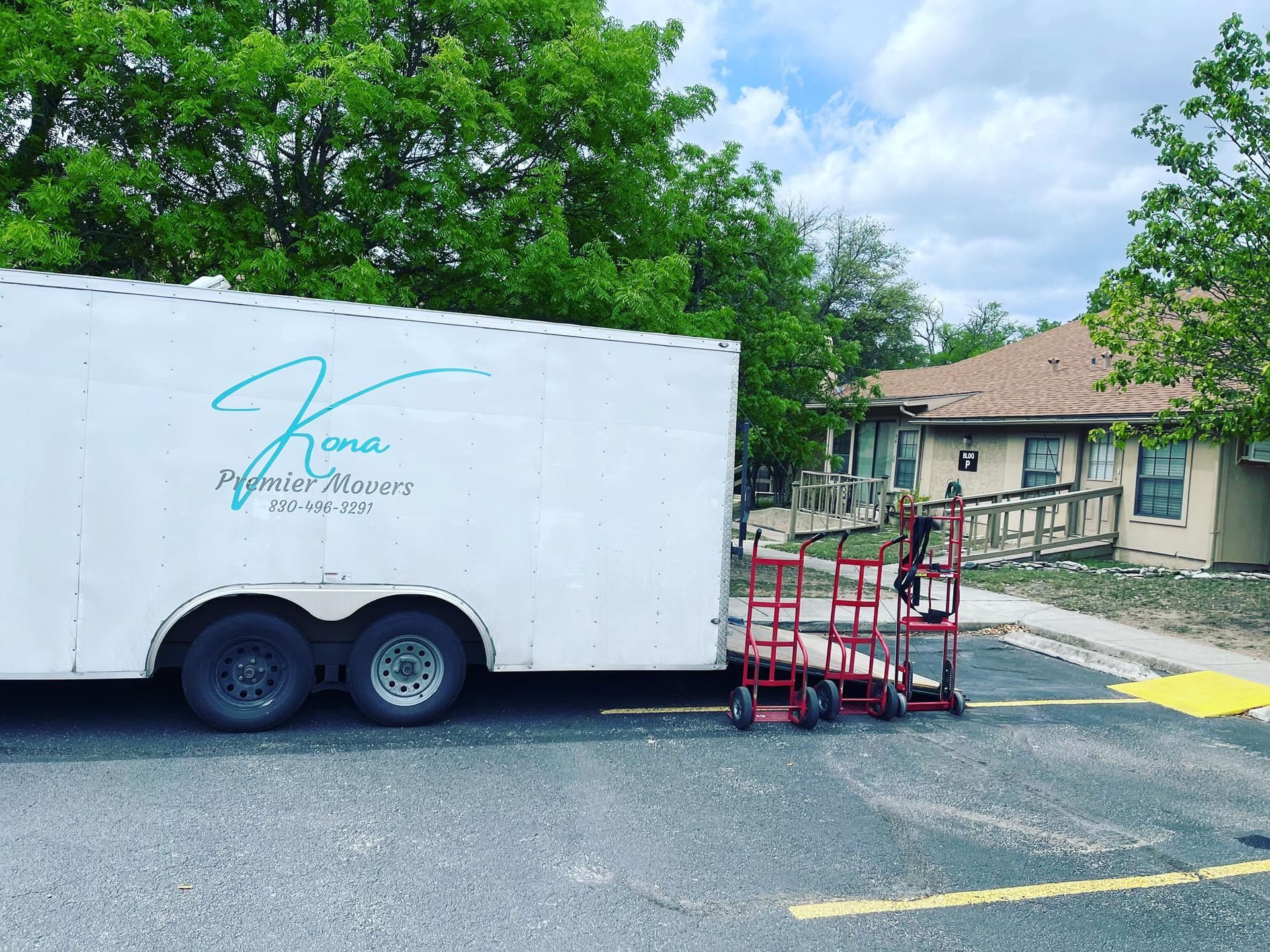 A white trailer is parked in a parking lot next to a house.