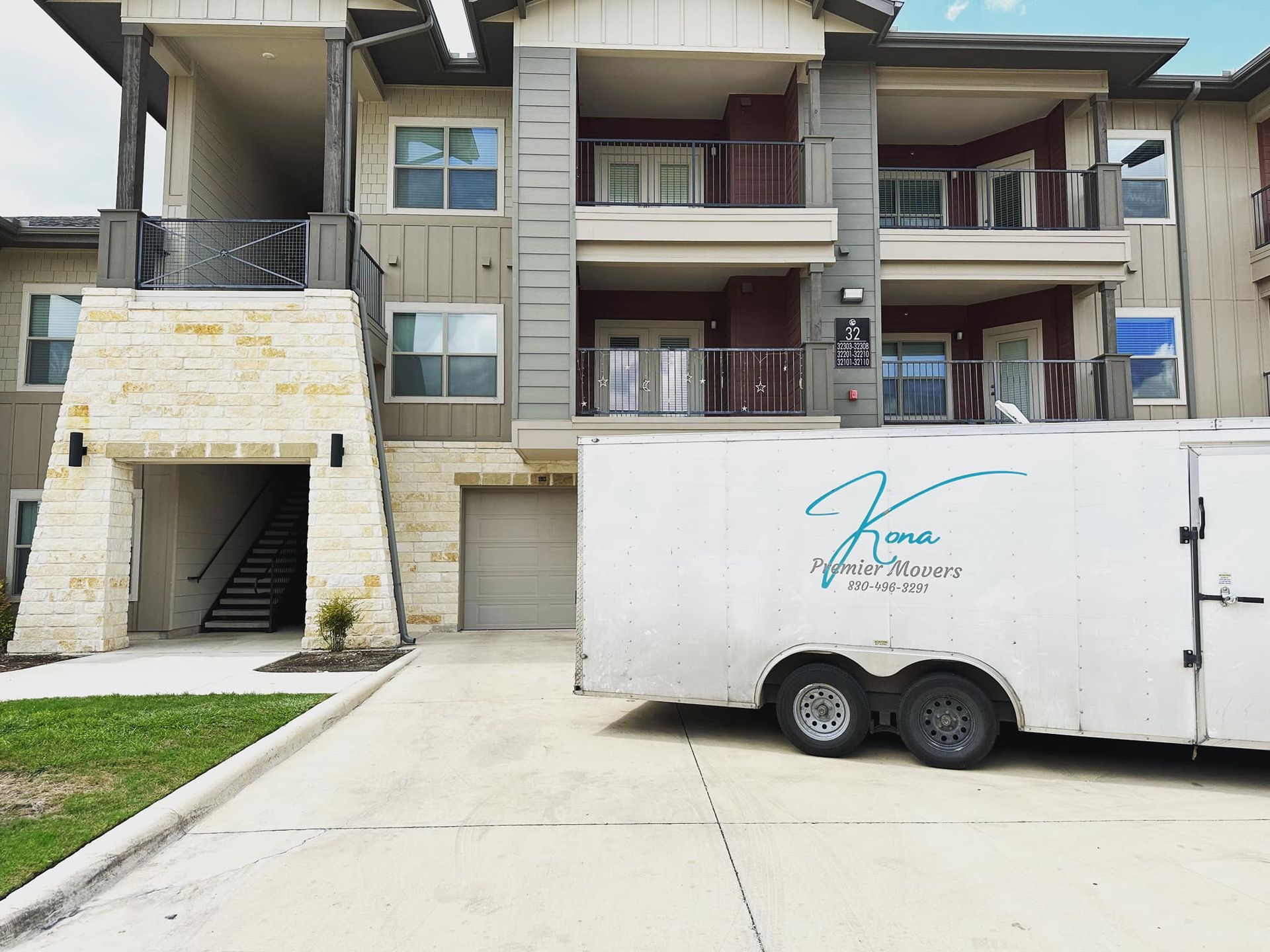 A white trailer is parked in front of a large apartment building.