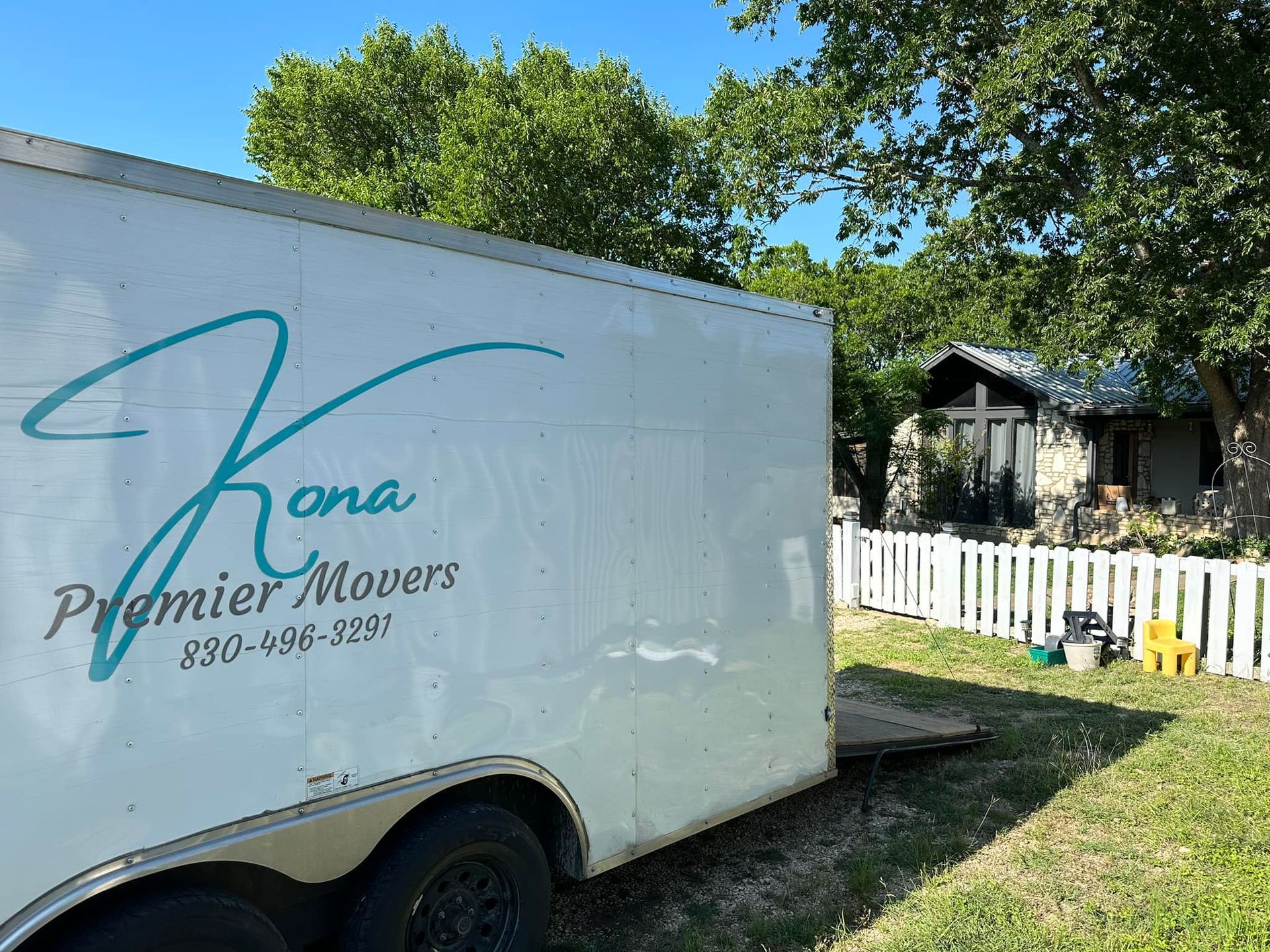 A white trailer from kona premier movers is parked in front of a house.