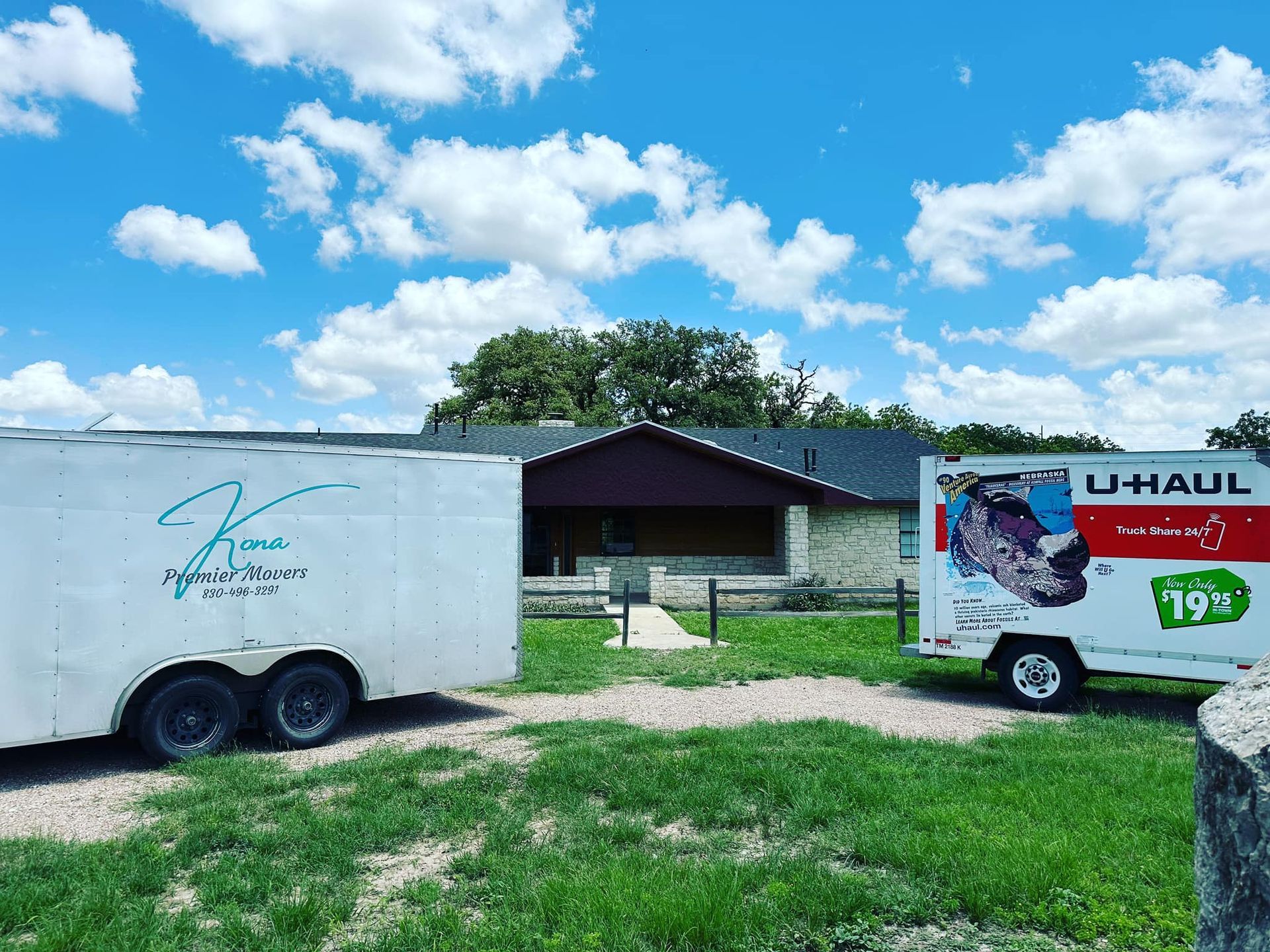 A uhaul truck is parked next to a trailer in front of a house.