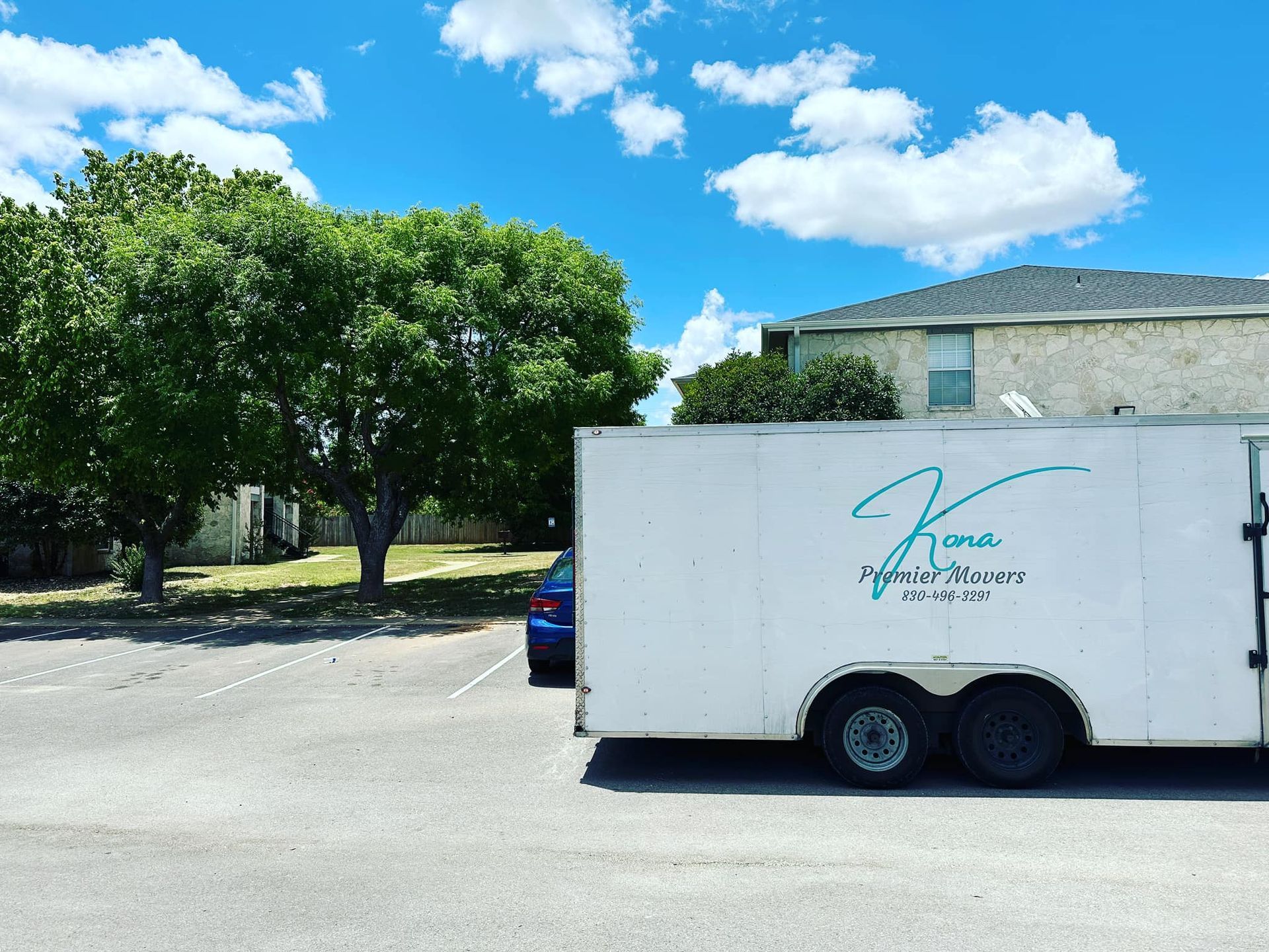 A white trailer is parked in a parking lot with trees in the background.