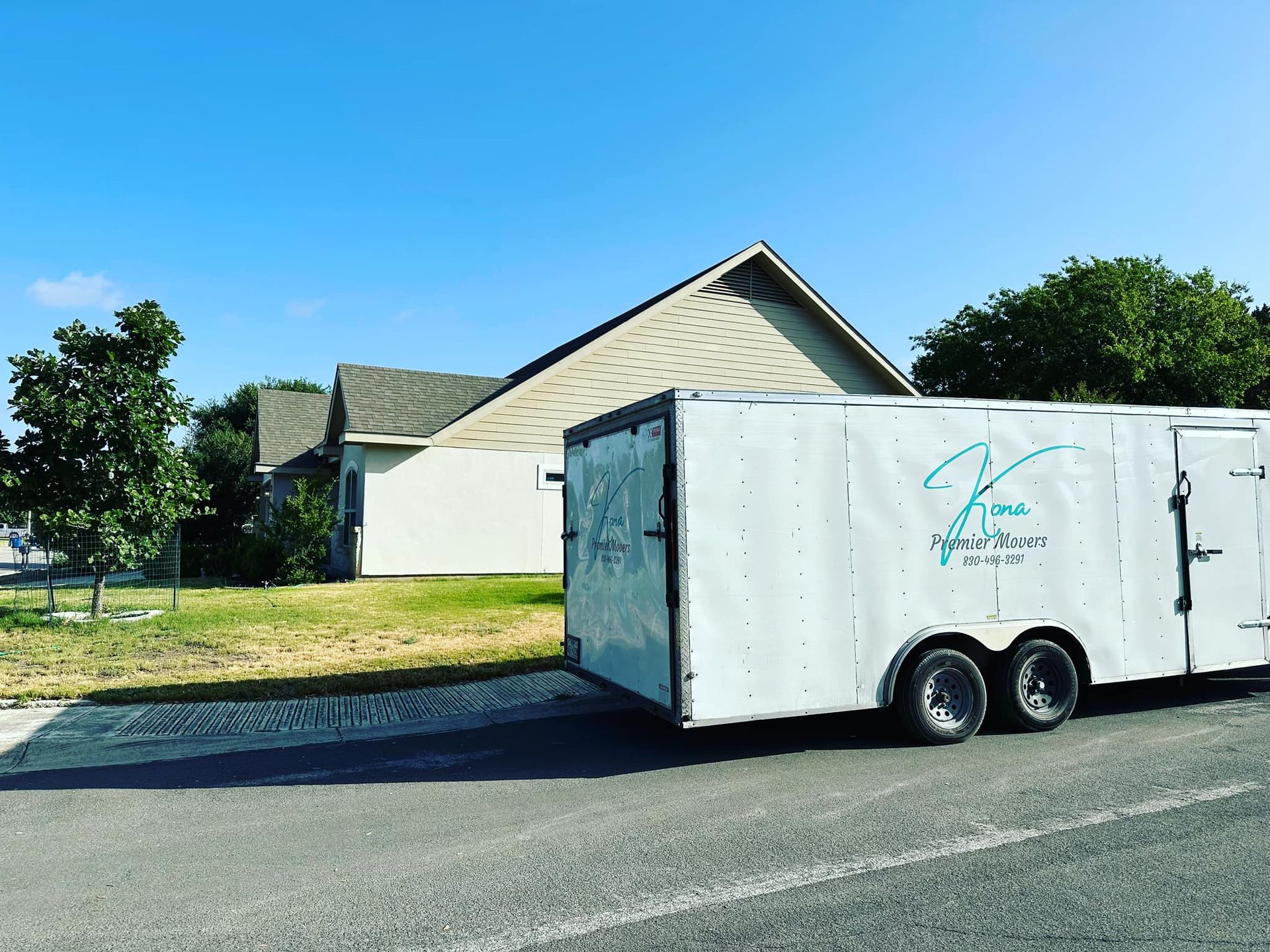 A white trailer is parked on the side of the road in front of a house.