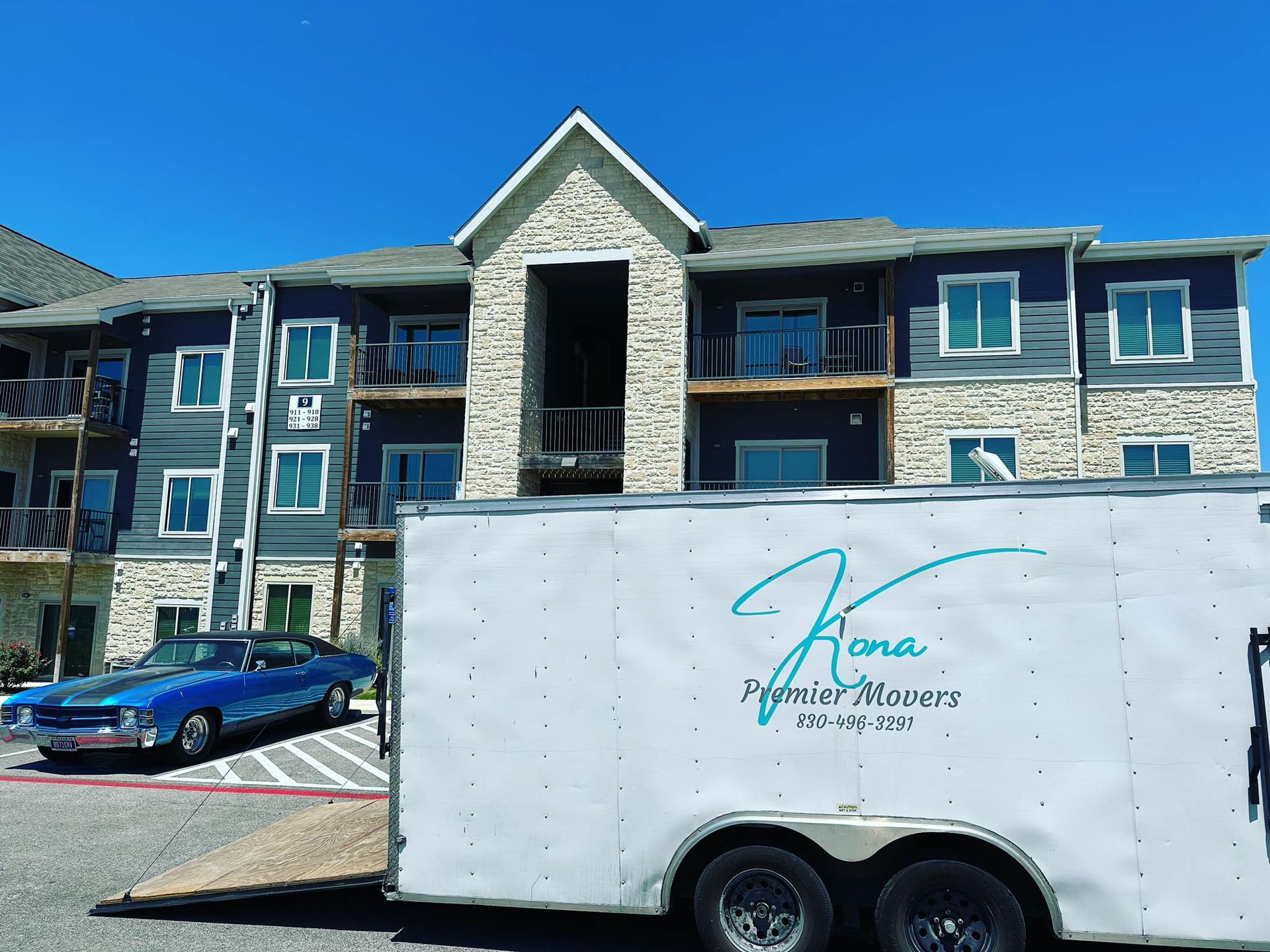 A white trailer is parked in front of a large apartment building