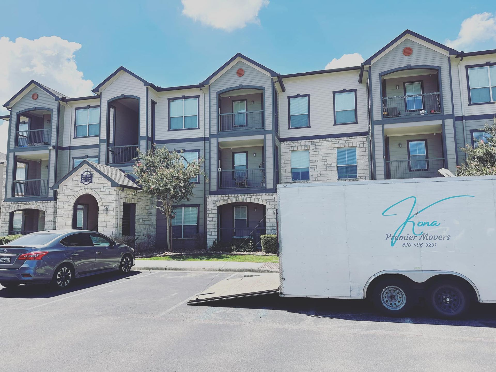 A white trailer is parked in front of a large apartment building.