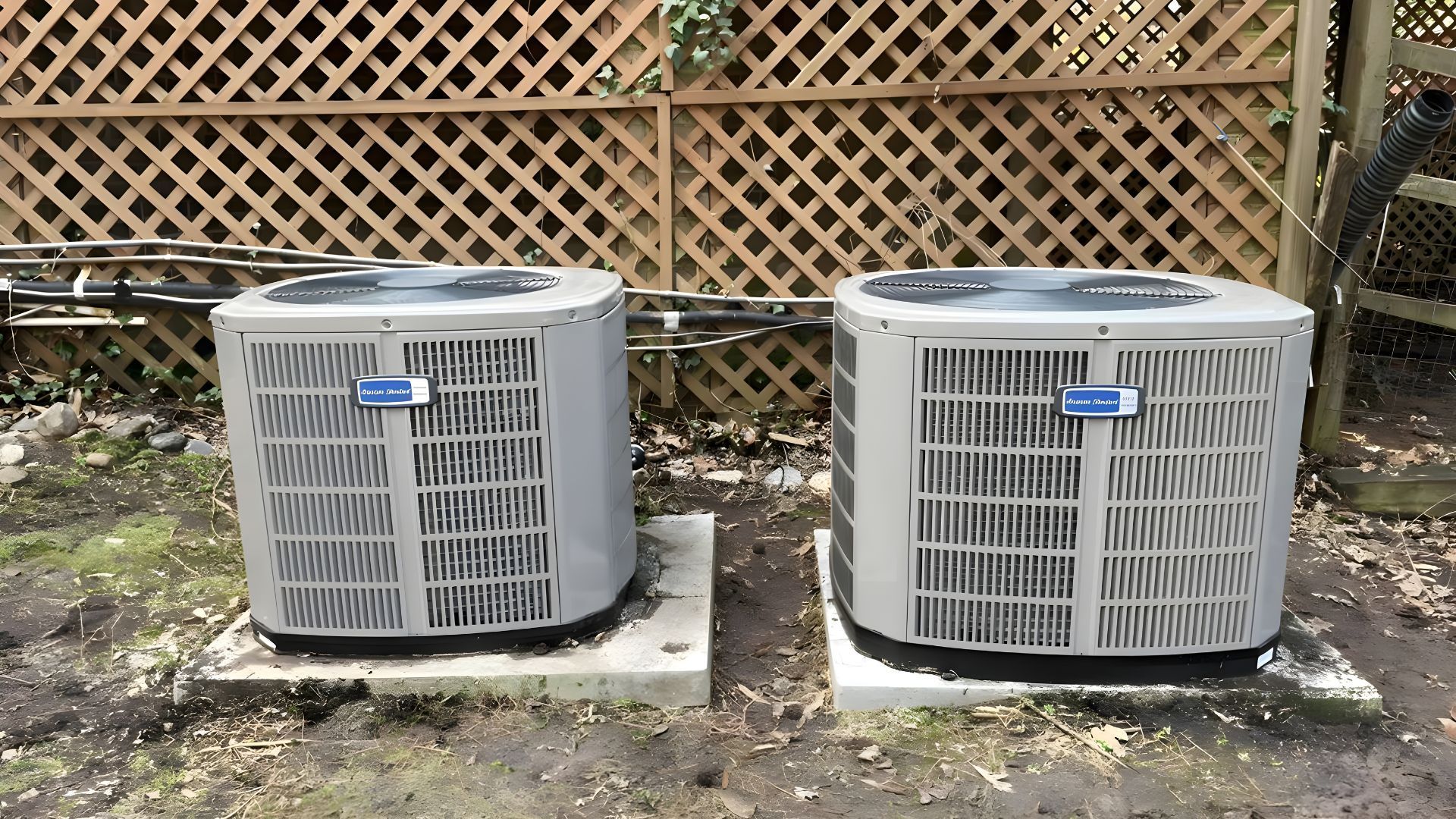 Two air conditioners are sitting next to each other in a backyard.