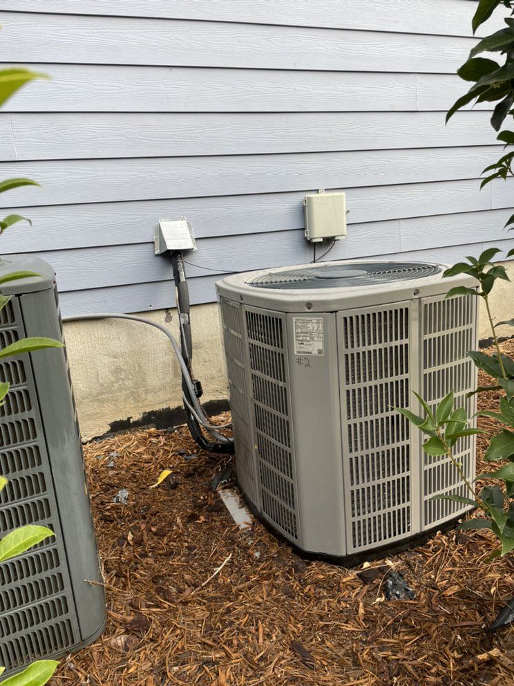 An air conditioner is sitting outside of a house next to a tree.