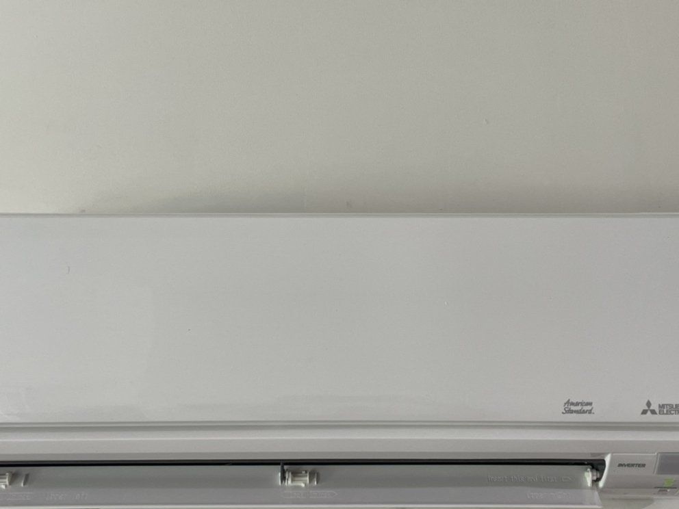 A white air conditioner is hanging on a white wall.
