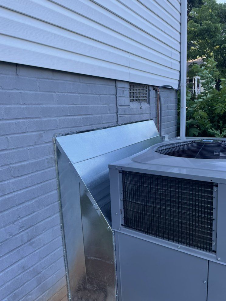 A gray air conditioner is sitting on the side of a house.
