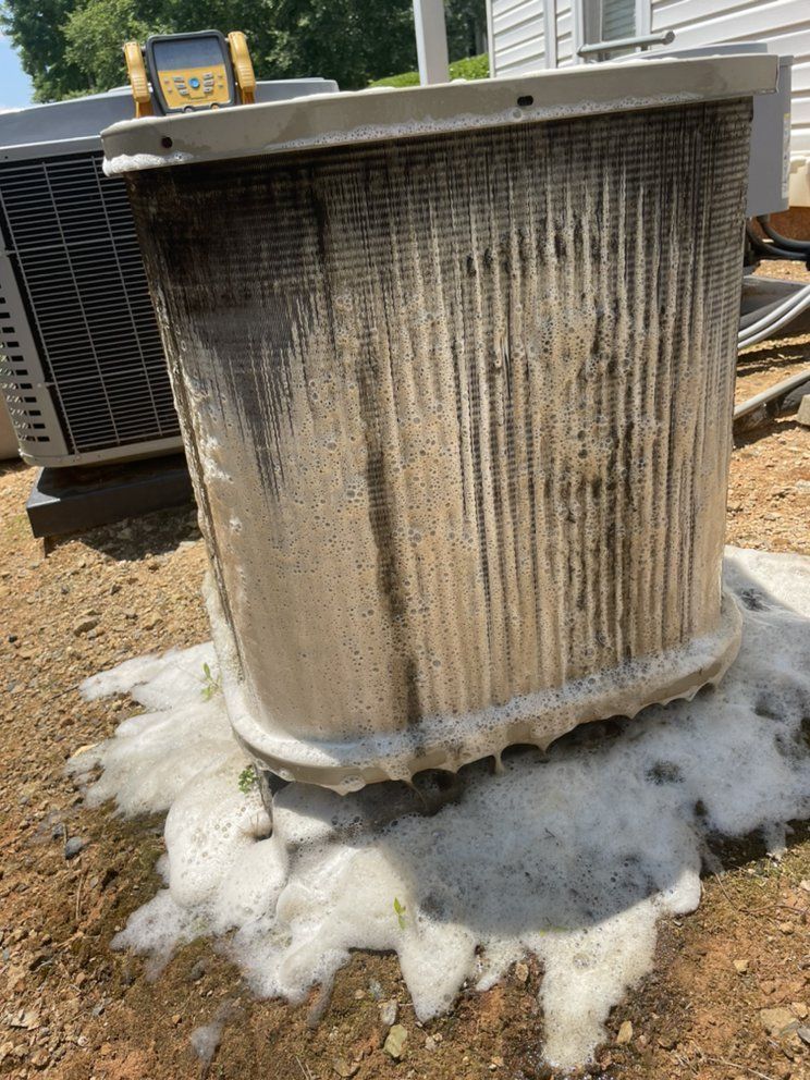A dirty air conditioner is sitting on the ground next to a house.