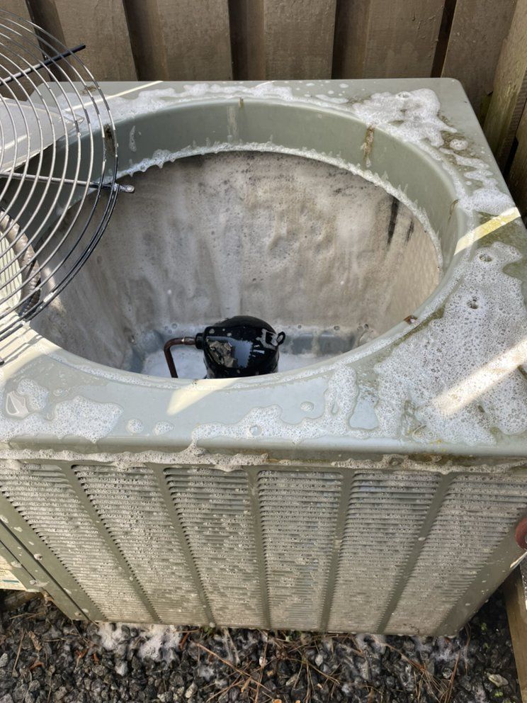 A dirty air conditioner is sitting on the ground next to a fence.