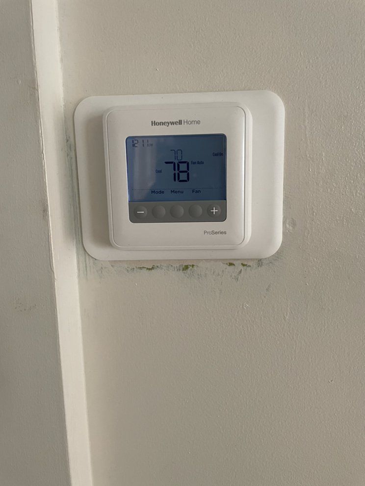 A white thermostat is mounted on a white wall.