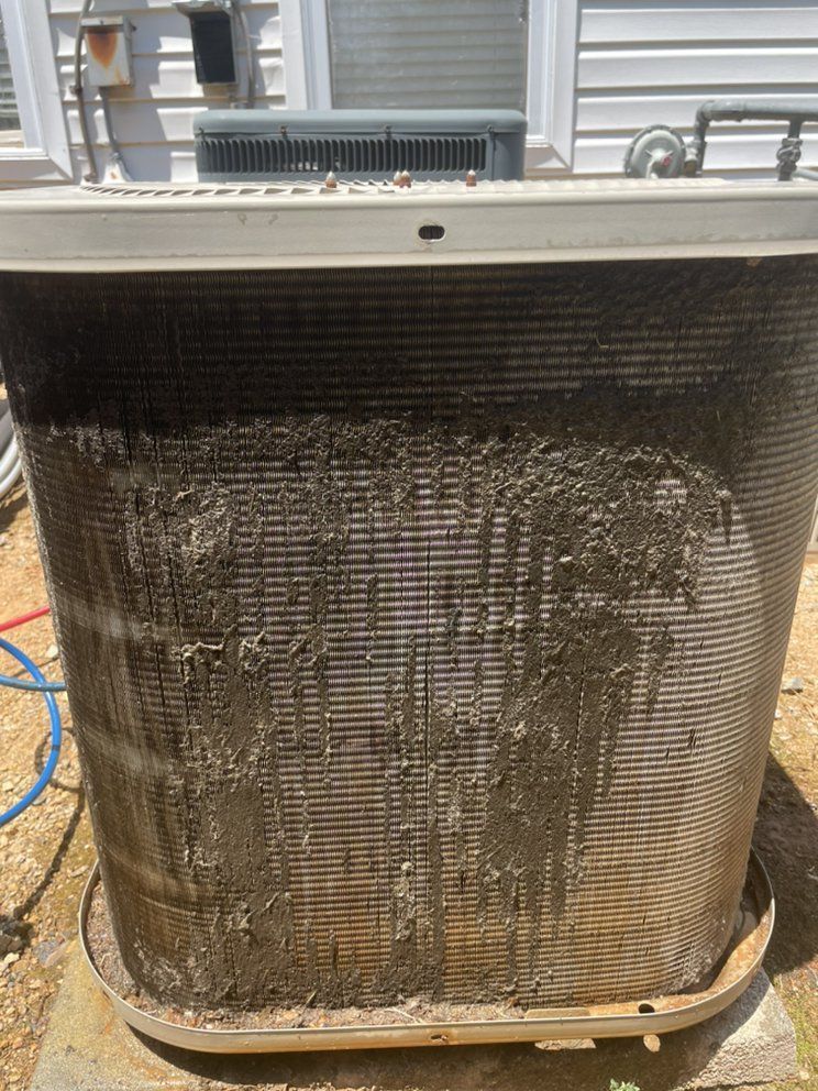 A dirty air conditioner is sitting on the ground in front of a house.