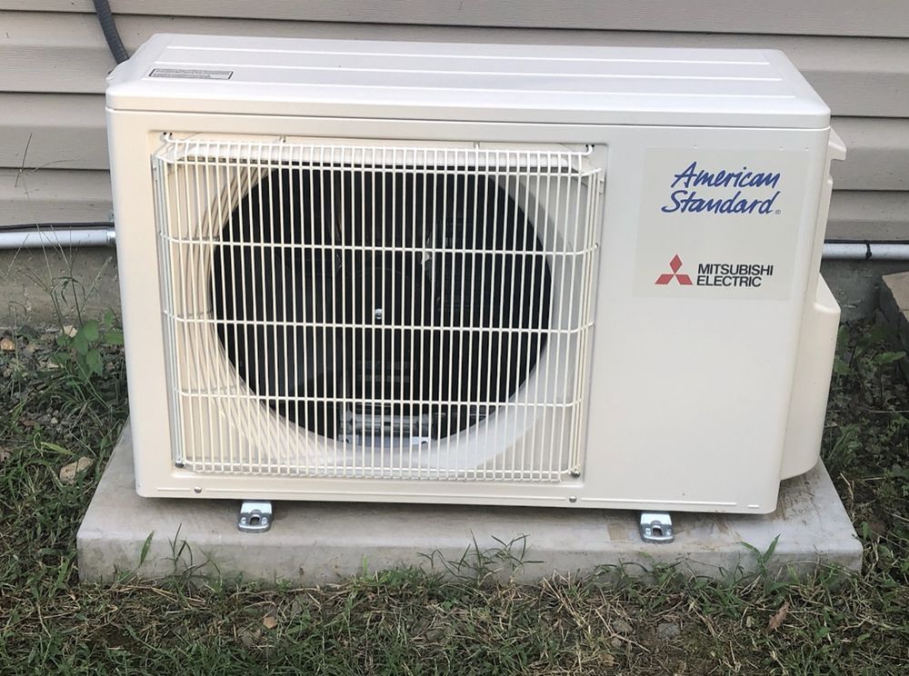 A white air conditioner is sitting on top of a concrete base.