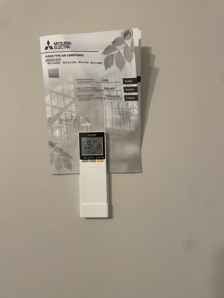 A remote control is hanging on a wall next to a manual.