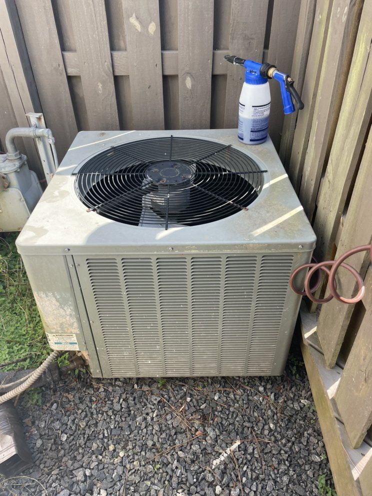 An air conditioner is sitting on the ground next to a fence.