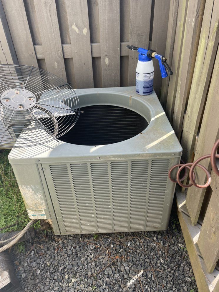 An air conditioner is sitting on the ground next to a fence.