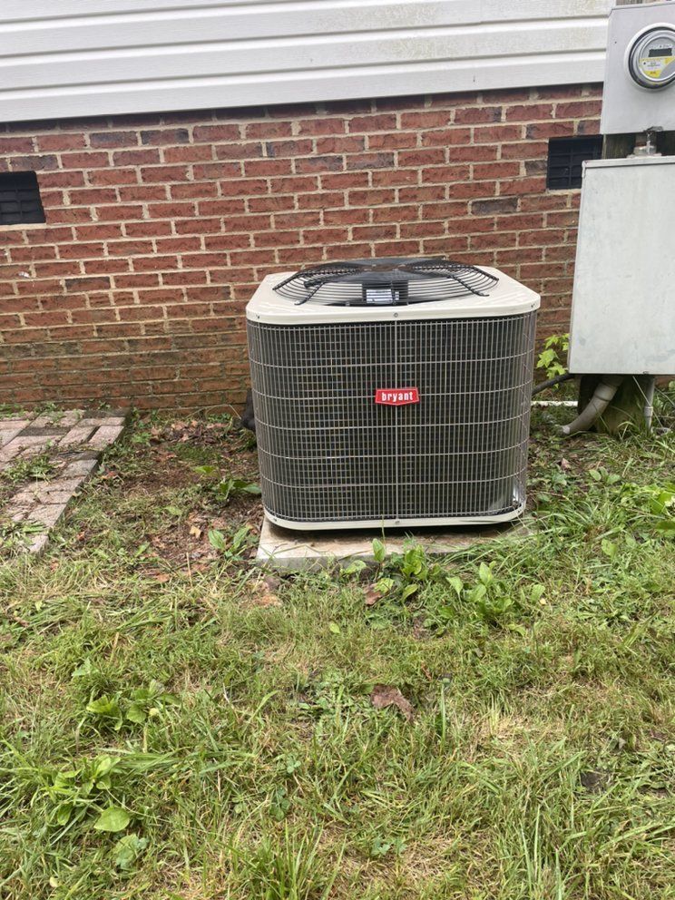 A large air conditioner is sitting in the grass in front of a brick building.