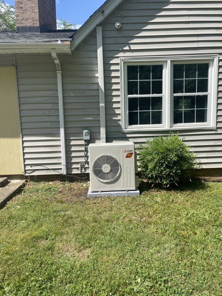 A large air conditioner is sitting on the side of a house next to a window.