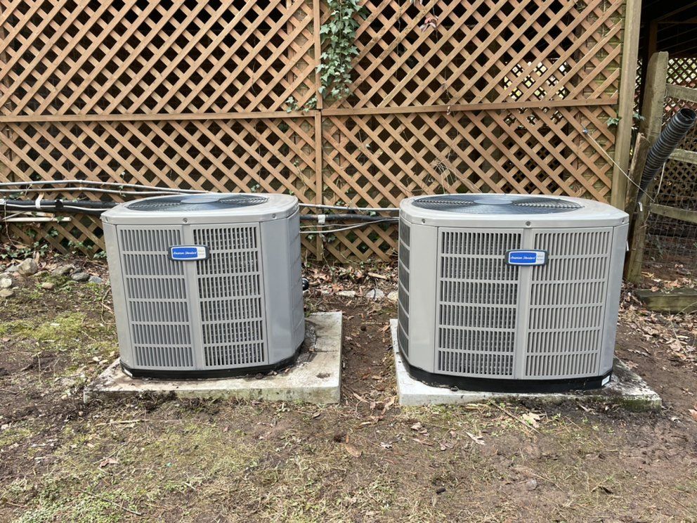 Two air conditioners are sitting next to each other in front of a wooden fence.