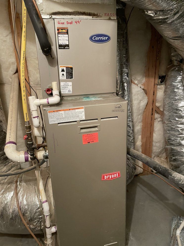 A carrier air conditioner is sitting in a basement next to pipes.