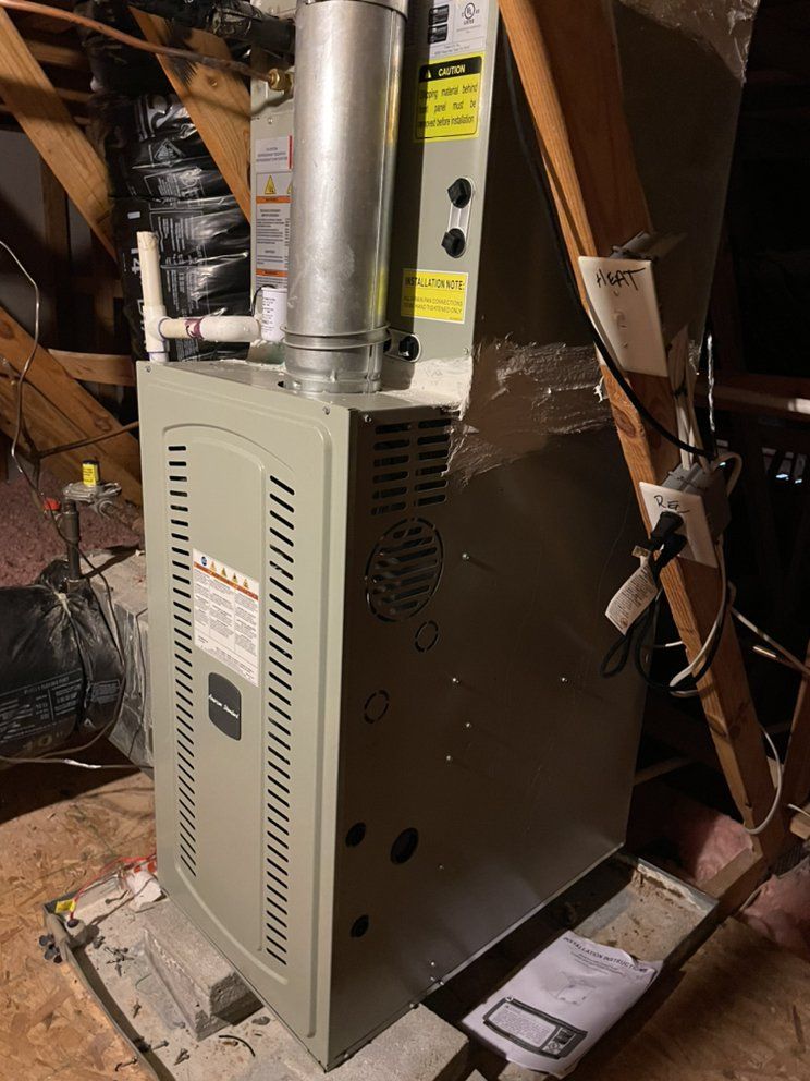 A gas furnace is sitting in the attic next to a ladder.