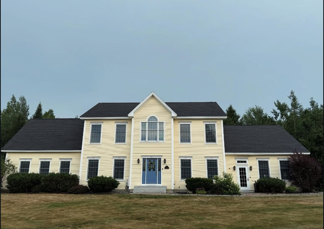 Yellow two-story house with black roof, blue door, and windows. Set on a grassy lawn.