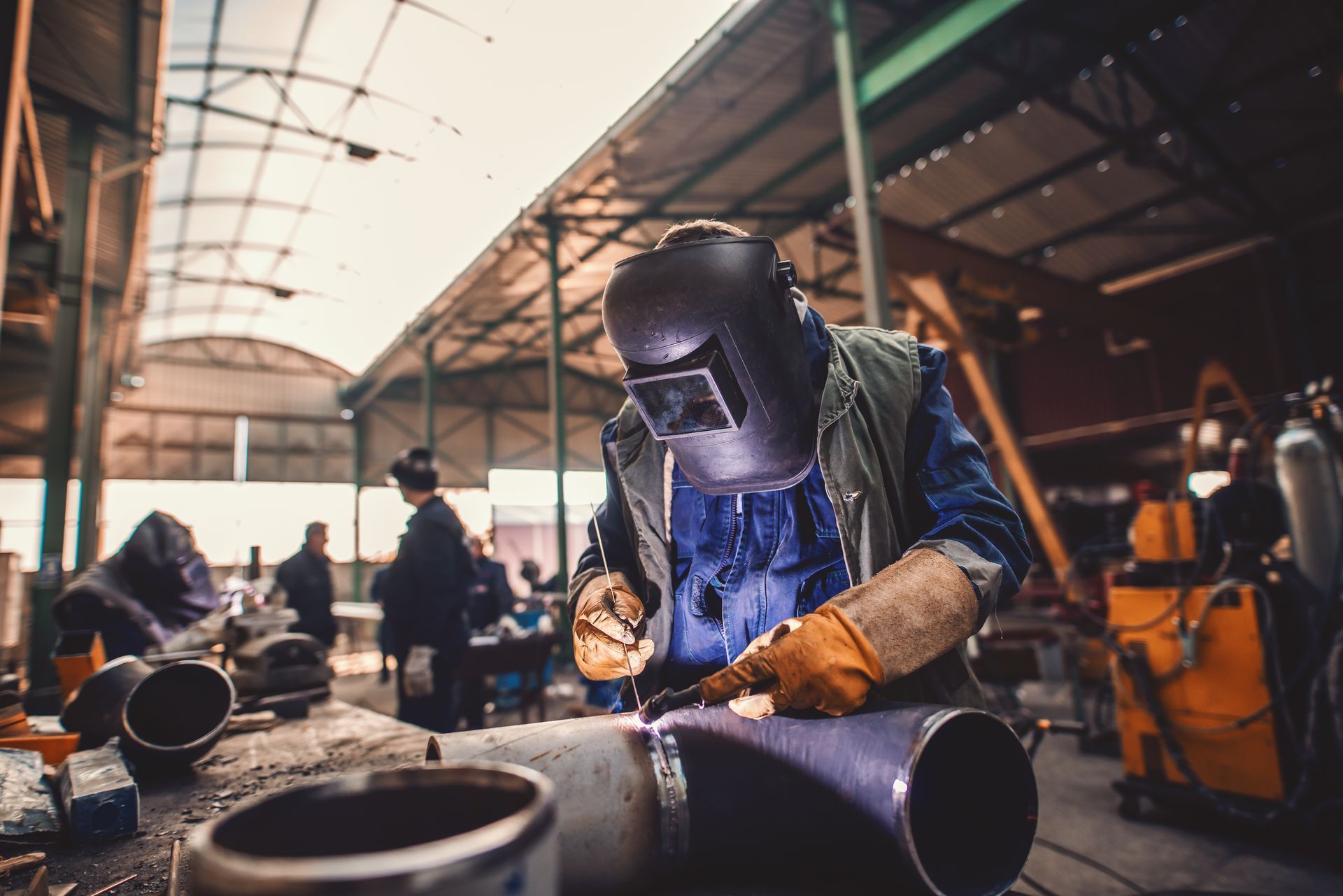 Un homme portant un casque de soudage soude un tuyau dans une usine.