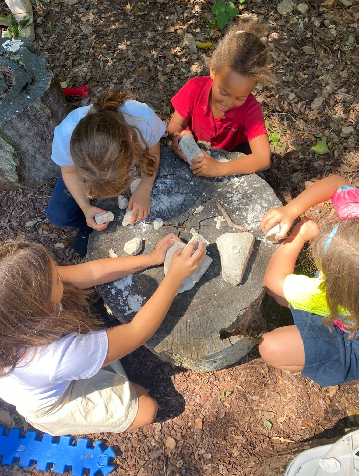 A group of children are sitting around a rock playing with rocks.