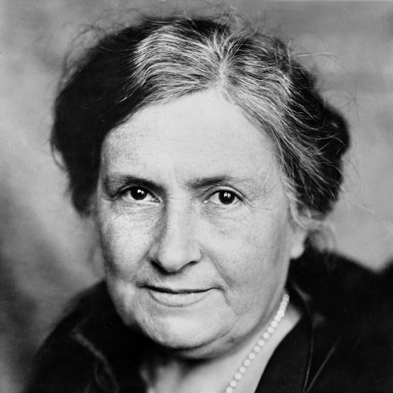 A black and white photo of an older woman wearing a pearl necklace.