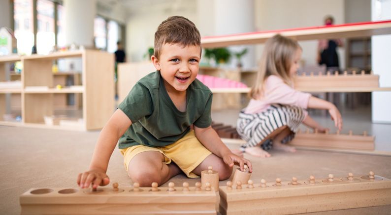 A boy and a girl are sitting on the floor playing with wooden blocks.