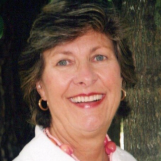 A woman wearing a white shirt and a pink necklace smiles for the camera