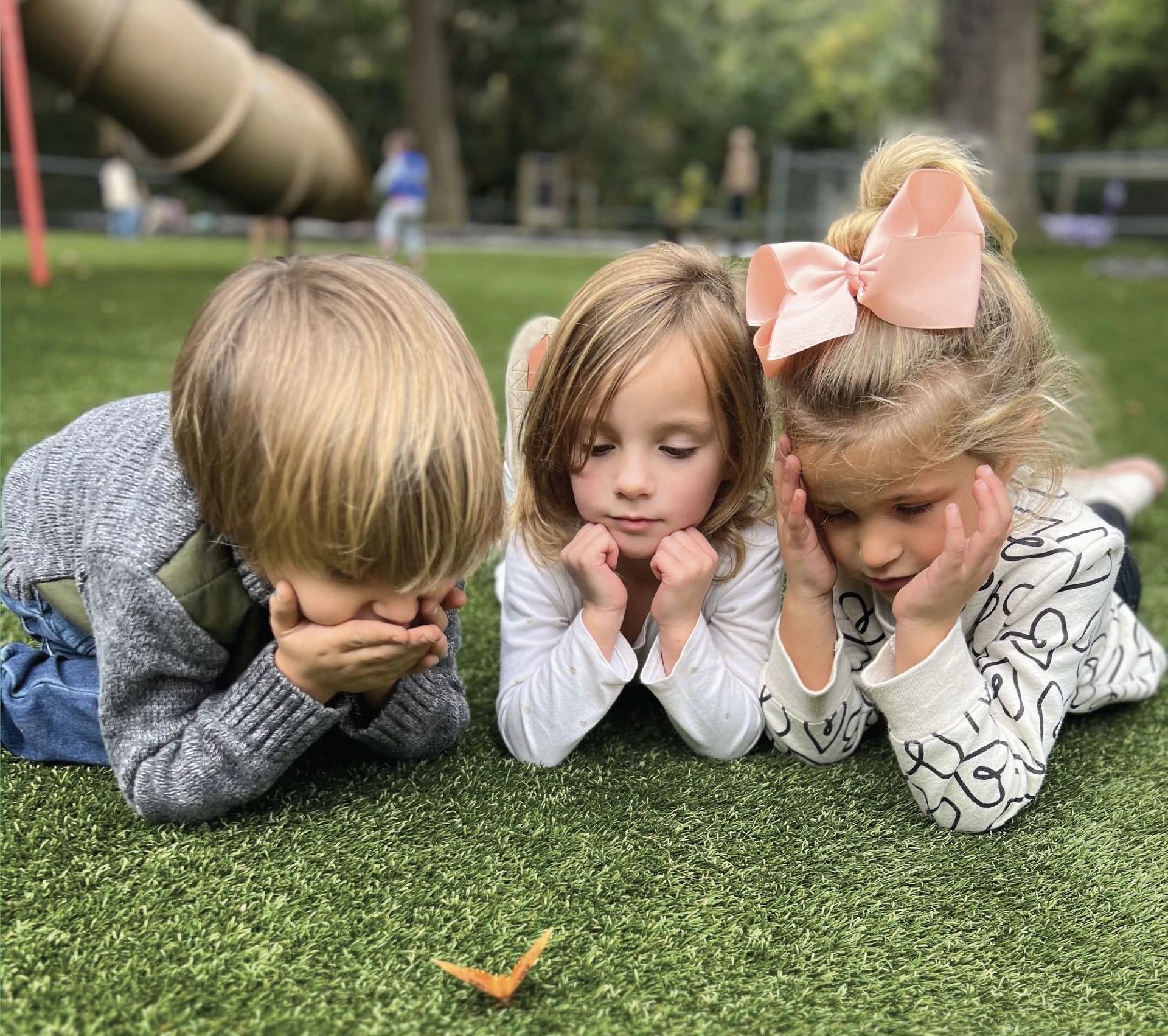 A boy and two girls are laying on the grass in a park.