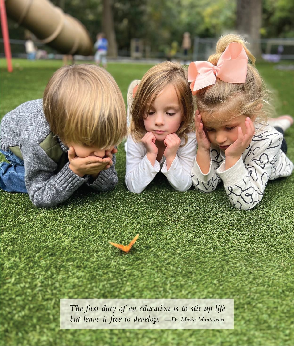 A boy and two girls are laying on the grass looking at a leaf.