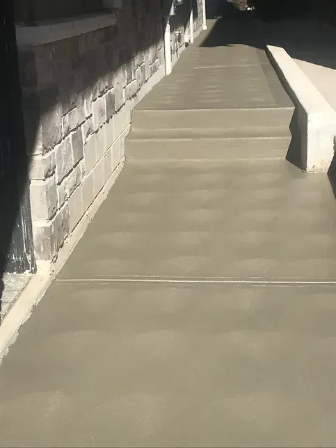 A concrete sidewalk next to a brick wall.