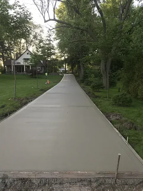 A concrete driveway leading to a house surrounded by trees and grass.