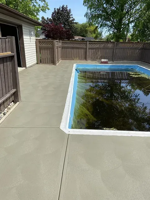 A large swimming pool is surrounded by a concrete patio and a wooden fence.