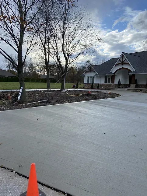 A concrete driveway with an orange cone in front of a house.