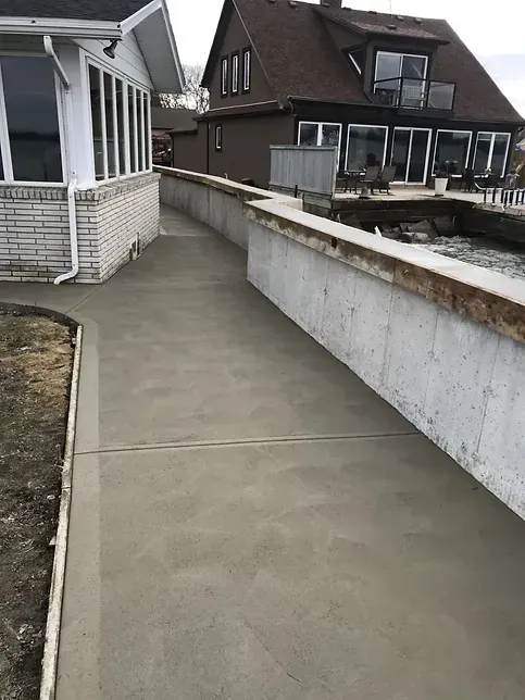 A concrete walkway leading to a house next to a body of water.