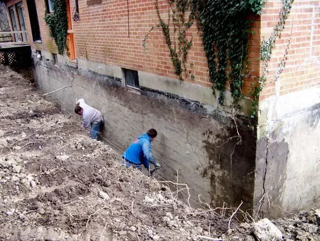 Two men are working on the side of a brick building.