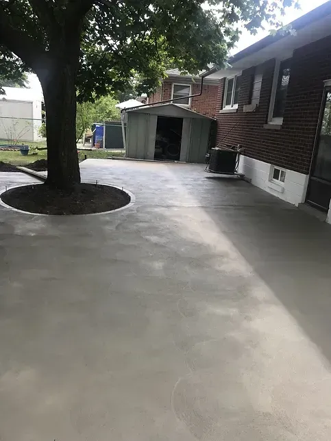 A concrete driveway in front of a brick house with a tree in the middle.