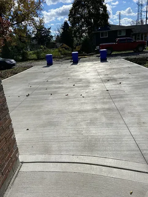 A concrete driveway with blue trash cans on it