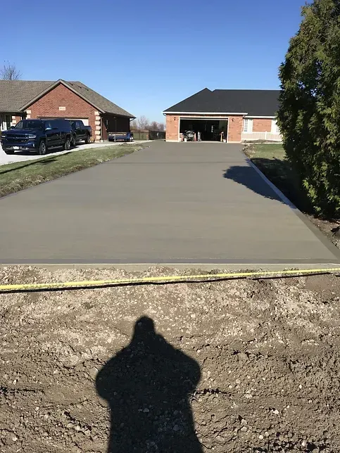 A shadow of a person is cast on a concrete driveway in front of a house.